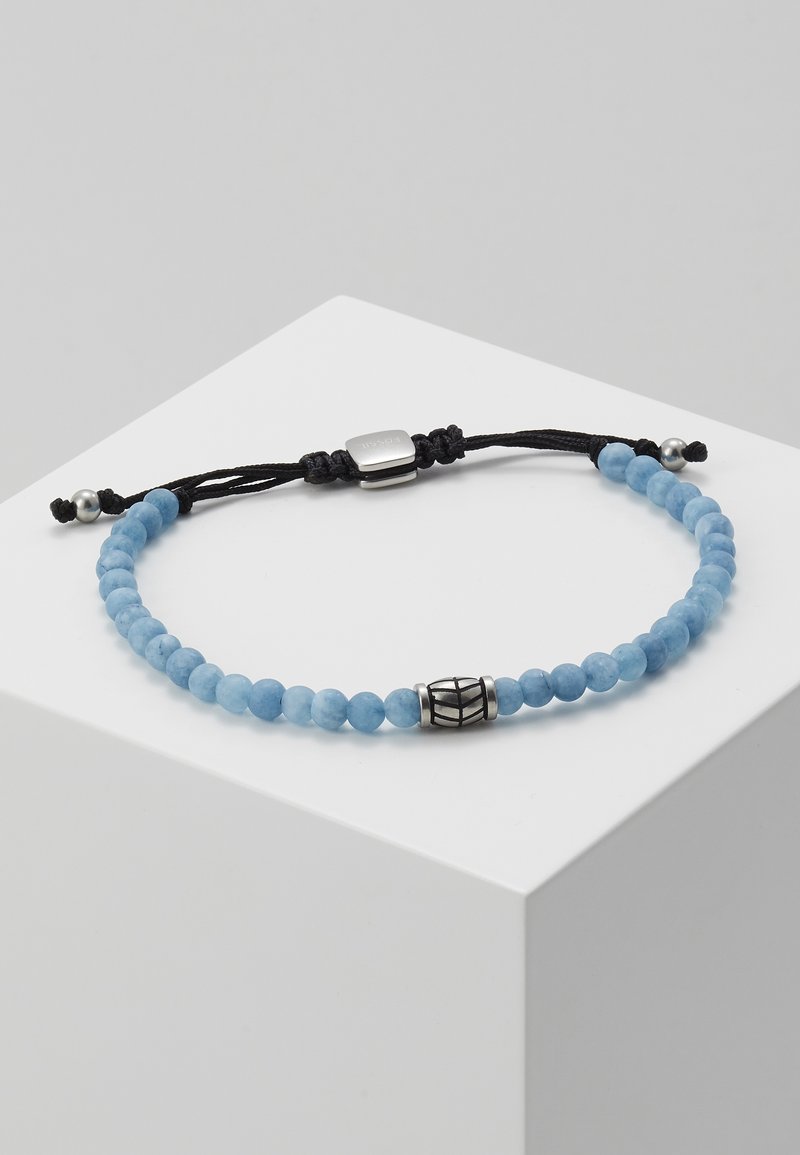 Bracelet ajustable avec de petites perles rondes bleues, une perle centrale argentée avec des lignes noires, un cordon noir et des fermoirs argentés sur une surface blanche.