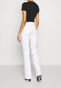 Białe dżinsy z wysokim stanem o luźnym kroju, pięcioma kieszeniami i widocznymi szwami, zestawione z dopasowaną czarną koszulką i czarnymi szpilkami.