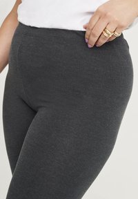 Grijze legging gemaakt van een glad, rekbaar materiaal met een elastische tailleband, featuring een nauwsluitende pasvorm en minimale details.