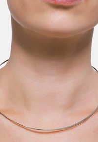 Halskette in Goldfarbe mit einem glatten, abgerundeten Design, das aus einer dünnen Drahtform besteht, die eng um den Hals sitzt.