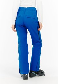Blauwe skibroek met een gladde textuur, zijritsen en een verstelbare taille, gecombineerd met zwarte skiskischoenen. Heeft een getailleerde pasvorm en een functioneel ontwerp.