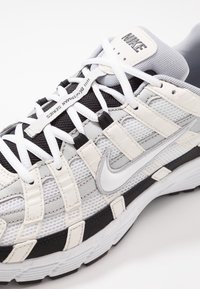 Tenisky Nike s šedou, bílou a černou síťovinou na svršku, vrstveným designem, plochými tkaničkami a texturovanou gumovou podrážkou.