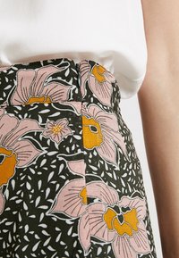 Blumiger Rock mit pinken und gelben Blumen auf dunklem Hintergrund, mit Reißverschluss, kombiniert mit einem weißen ärmellosen Oberteil, sichtbarer Arm auf der rechten Seite.