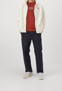 Vit fleece zip-up jacka över en röd Nike grafisk t-shirt, ihop med marinblå cargobyxor och ljusgrå Nike sneakers. Avslappnad outfit.