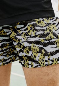 Kupanje šortsevi u šarenom uzorku s prugama u žutoj, crnoj i bijeloj boji, uz dodatak točkica. Izrađeni od laganog, prozračnog materijala.