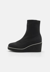 Bottes chelsea noires à talon compensé avec une tige en tricot extensible, bout rond et semelle épaisse. Présente un contour gris contrastant le long de la base.