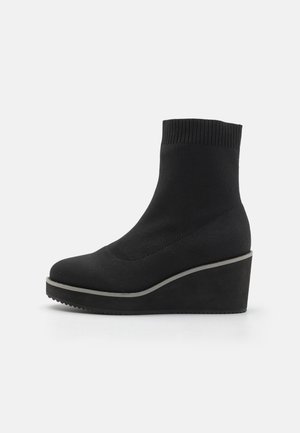 Black wedge ankle boots with a stretchy knit upper, rounded toe, and thick sole. Features a contrasting gray trim along the base.