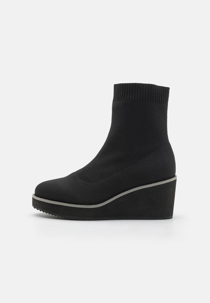 Bottes chelsea noires à talon compensé avec une tige en tricot extensible, bout rond et semelle épaisse. Présente un contour gris contrastant le long de la base.