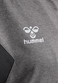 Grijs textiel met een gestructureerd gaaspatroon. Er is een witte logo weergegeven met een bij-ontwerp en het woord "hummel" eronder.