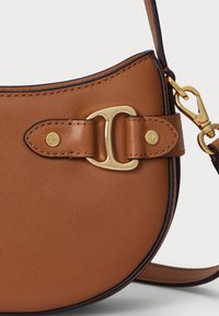 Ruda odinė rankinė su išlenktu pavidalu, auksinės spalvos aparatinė įranga ir dekoratyvių sagtelių uždarymu. Lygi tekstūra su kontrastingais akcentais.