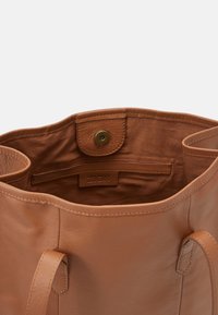 Sac fourre-tout en cuir beige avec une texture lisse, ouverture sur le dessus et poche intérieure ; dispose d'une fermeture à pression et de détails de couture discrets.