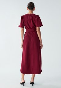 Burgundijas midi kleita ar īsām pūkainām piedurknēm, pieguļošiem gurniem un plūstošu siluetu. Izgatavota no gludas auduma ar slēptu aizmugurējo rāvējslēdzēju.