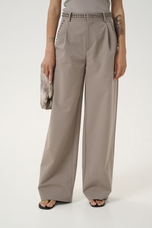 Hellbraune weit geschnittene Hose mit hoher Taille, die silberne Nietendetails entlang des Gürtels und der Seitennähte aufweist, kombiniert mit einer strukturierten Clutch.