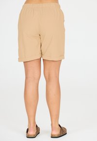 Beiga shorts med elastiskt midjeband och vikta kanter, tillverkade av lätt tyg, med två sidofickor och bärs med bruna sandaler.