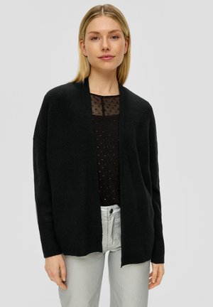 Schwarze Strickjacke mit offenem Vorderteil, geripptem Muster und langen Ärmeln, kombiniert mit einem schwarzen durchsichtigen Oberteil mit kleinen gestickten Punkten.