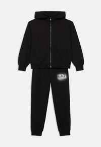 Črna majica s kapuco z zadrgo in dvema stranskima žepoma, združena s črnimi trenirkami s srebrnim logotipom EA7 na stegnih.