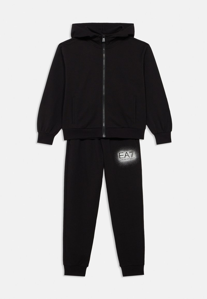 Črna majica s kapuco z zadrgo in dvema stranskima žepoma, združena s črnimi trenirkami s srebrnim logotipom EA7 na stegnih.