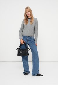 Grijze gebreide trui, high-waisted vervaagde blauwe jeans en een zwarte handtas met textuur en gathered handvatten. Zwarte schoenen maken de outfit compleet.