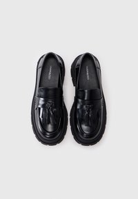 Zwarte leren loafers met kwastdetail, ronde neus en dikke rubberen zool. Gladde afwerking en subtiele stiksels.