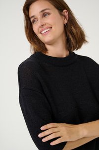 Black knitted sweater with a high neckline, short sleeves, and a textured pattern. The fabric appears soft and breathable.