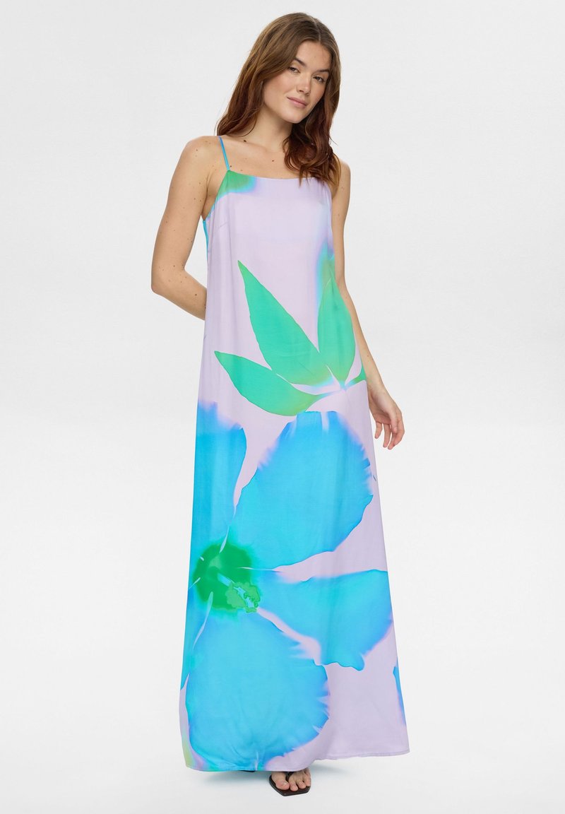 Mujer con vestido maxi lavanda sin mangas con gran estampado floral azul y verde, de pie frente a un fondo blanco liso.
