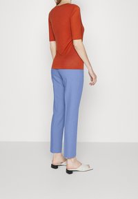 Rostfärgad åtsittande topp med korta ärmar; ljusblå skräddarsydda byxor med rak passform; vita öppna sandaler med svarta klackar.