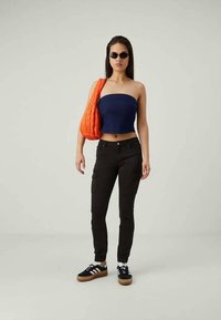 Navy strapless top, black cargo pants, and black sneakers with white stripes. Bright orange bag, sleek sunglasses, and straight long hair.