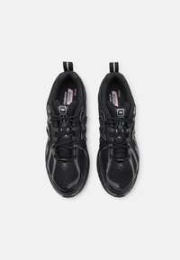Baskets de sport noires avec une tige en mesh, une semelle texturée et des accents réfléchissants. Elles présentent un design à lacets et des anses au niveau du talon.