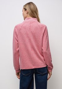 Rosa, strukturierter Pullover mit hohem Kragen und gerippten Bündchen, kombiniert mit dunkelblauen Jeans. Hat eine lockere Passform und Raglanärmel.