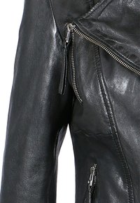 Schwarze Lederjacke mit einer leicht gelebten Textur, Reißverschlusstaschen und asymmetrischem Frontreißverschluss. Mit silbernen Beschlägen akzentuiert.