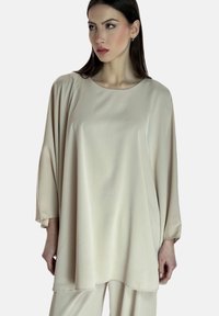 Tunik in tessuto beige, fluida, con maniche lunghe e scollo tondo, realizzata in un materiale leggero e morbido. Design minimalista, senza motivi visibili.