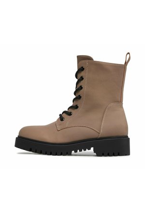 Kampfboot aus cognacfarbenem Leder mit schwarzen, dicken Gummisohlen und Zuglasche an der Rückseite, von der Außenseite gezeigt.