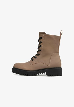 Brązowy skórzany botek wojskowy na sznurówki z czarną grubą gumową podeszwą i pętelką z tyłu, widoczny z zewnętrznej strony.