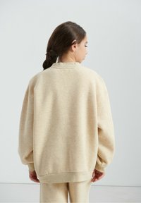 Sweat-shirt beige surdimensionné avec un col rond, des épaules tombantes et des poignets côtelés. Texture douce avec un effet chiné subtil.