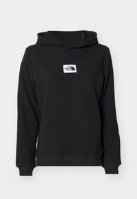 Felpa nera con cappuccio, texture a coste, patch logo bianco sul fronte e polsini aderenti. Il materiale sembra morbido e flessibile.