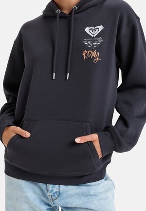 Czarna bluza z kapturem z przednią kieszenią i sznurkami, z białym i brązowym logo "Roxy" na piersi, noszona z jasnoniebieskimi dżinsami.