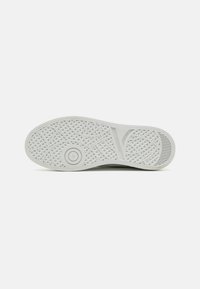 Weiße Sneaker-Sohle mit einem strukturierten, geometrischen Profil, das kreisförmige und diamantartige Formen umfasst, entworfen für Grip und Langlebigkeit.