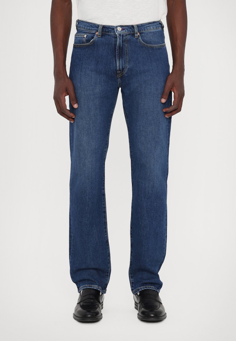 Jean en denim bleu à jambe droite avec un design classique à cinq poches, des détails de couture subtils et une taille mi-haute.
