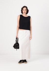 Svart cropped tank topp, hvit maxi skjørt med snøring, svart blomstrete snørepose, svarte sneakers med kremfarget såle. Glatt tekstur, moderne design.