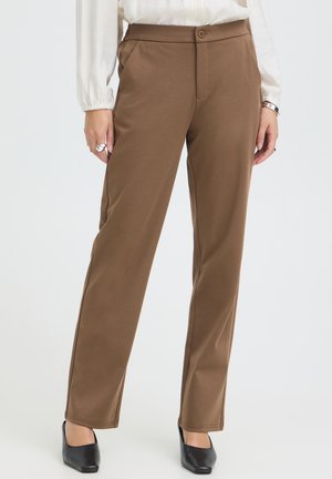 Pantalon marron droit avec poches latérales porté avec des chaussures à talons noires et un haut blanc à manches longues.