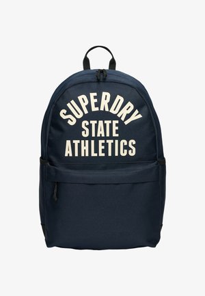 Granatowy plecak z przednią kieszenią na zamek i białym napisem "SUPERDRY STATE ATHLETICS" na głównym kompartmencie.