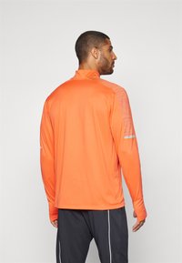 Long-sleeve athletic shirt in bright orange, lightweight fabric, mock neck, subtle texture on shoulders, reflective accents on sleeves.