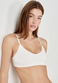 Bralette blanca con tirantes ajustables, fabricada en tejido suave y con un diseño clásico de escote en V, que presenta una banda inferior sin costuras y hardware mínimo.