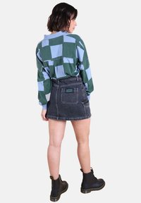 Chemise surdimensionnée verte et bleue à motifs avec des épaules tombantes, associée à une jupe en denim noir avec une poche arrière et un détail de logo.