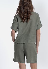 Top a maniche corte in lino verde oliva e pantaloni abbinati. Vestibilità rilassata con maniche arrotolate e un finish leggermente testurizzato. Design minimalista.