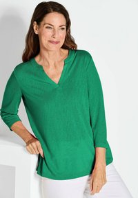Grünes, V-Shirt aus weichem Material mit Dreiviertelärmeln. Das Design bietet eine lockere Passform und eine glatte Textur.