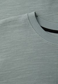 Pull à col rond en tissu côtelé vert clair avec des coutures détaillées sur l'épaule et le col.