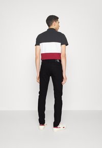 Polo de manga corta en rayas negras, blancas y rojas, combinado con jeans negros y zapatillas blancas. Presenta un cuello clásico y detalles del logo.