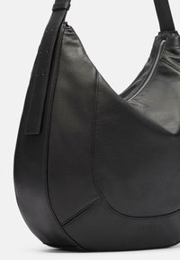 Sac à main noir en cuir avec une forme courbée et décontractée. Il dispose d'une fermeture zippée et d'une texture lisse, rehaussée de détails de couture subtils.