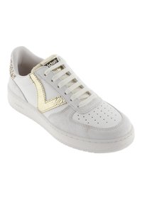 Sneaker bianco con una finitura testurizzata, accenti dorati sul logo e sul lato, lacci piatti e punta perforata per la ventilazione.